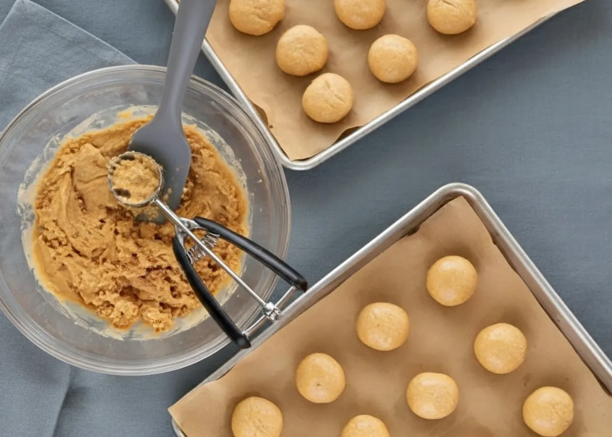 Scooping and rolling no-bake 3-ingredient peanut butter balls onto a parchment-lined tray